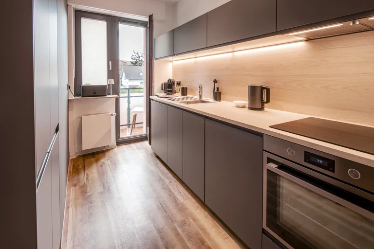 Helle, moderne Küche mit grauen Schränken, Holzarbeitsplatte und Tür zum Balkon.