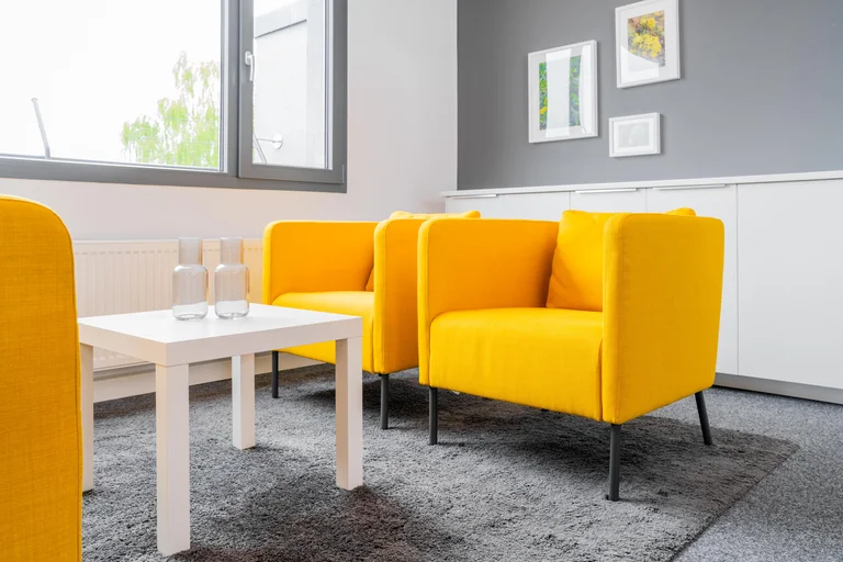 Freundlicher Aufenthaltsraum mit gelben Sesseln, grauem Teppich und hellgrauer Wandgestaltung in modernem Stil.