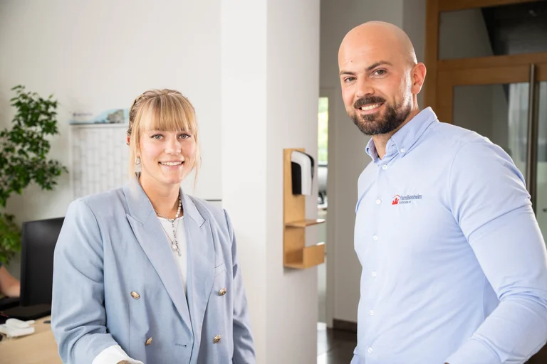 Zwei Mitarbeitende der Familienheim Karlsruhe eG stehen im Büro und lächeln freundlich in die Kamera.