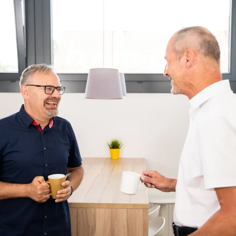 Zwei Mitarbeitende stehen im Büro und führen ein freundliches Gespräch bei einer Tasse Kaffee.