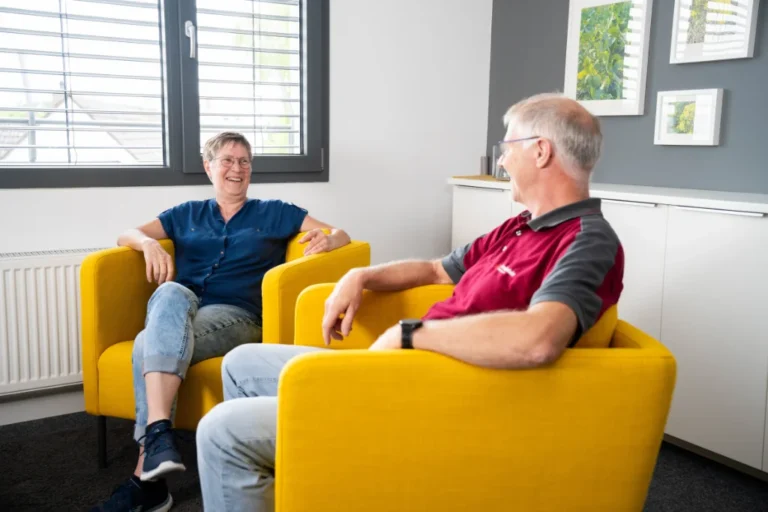 Zwei Mitarbeitende sitzen in gelben Sesseln und führen ein freundliches Gespräch in einem hellen Büro.