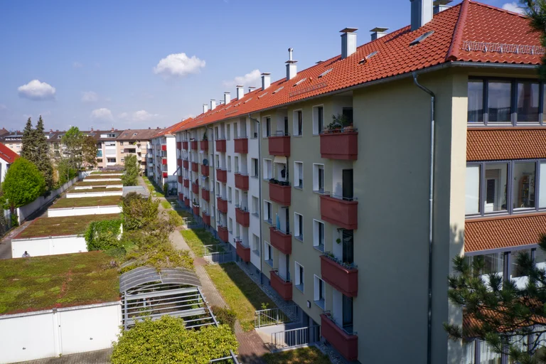 Wohnanlage der Familienheim Karlsruhe eG mit roten Balkonen und begrünten Garagendächern bei Sonnenschein.
