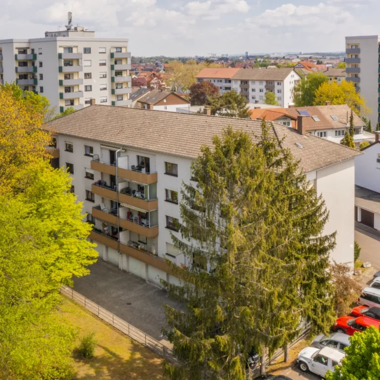 Gepflegtes Mehrfamilienhaus mit Balkonen in grüner Wohnlage, umgeben von Bäumen und weiteren Wohngebäuden.