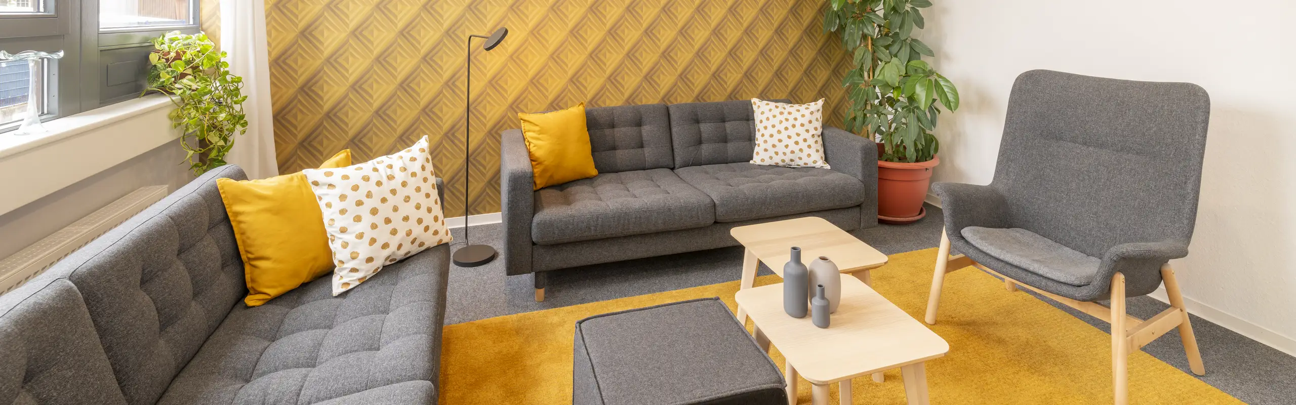 Heller Aufenthaltsraum mit grauen Sofas, gelben Kissen und modernen Holzmöbeln im Büro.