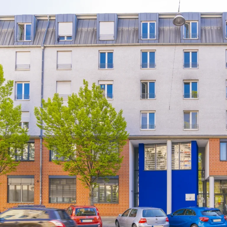 Modernes Mehrfamilienhaus mit teilweiser roter Klinkerfassade, großen Fenstern und markantem blauen Eingangsbereich.