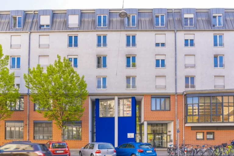 Modernes Mehrfamilienhaus mit teilweiser roter Klinkerfassade, großen Fenstern und markantem blauen Eingangsbereich.