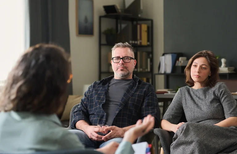 Zwei Personen sitzen in einem Raum und sprechen mit einer dritten Person in einem Beratungsgespräch.